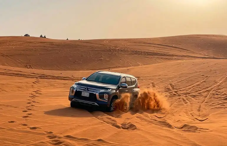 Blue SUV dune bashing through vibrant red sand dunes in Riyadh Red Sand Desert, Saudi Arabia
