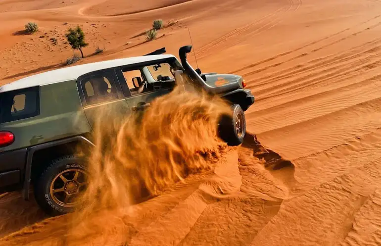 Green off-road vehicle powerfully driving through deep red sand dunes in Riyadh Red Sand Desert