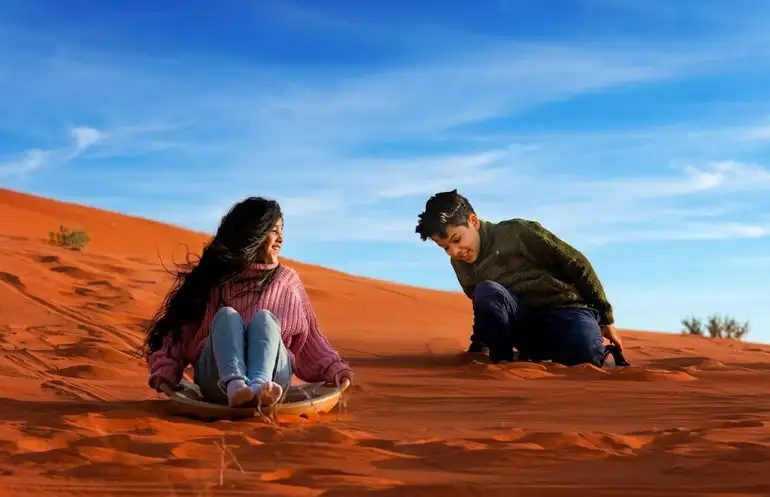 Kids enjoying sand sliding on the beautiful red sand dunes of Riyadh. A fun and safe family activity during the Red Sand Tour in Riyadh.