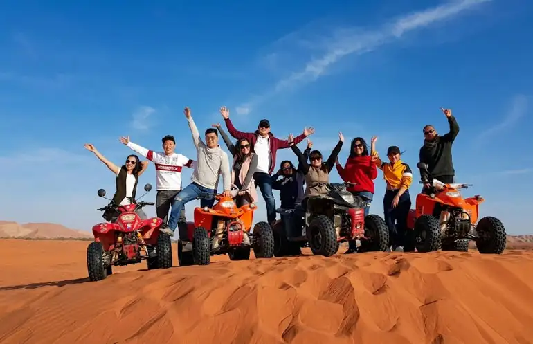 Smiling family and friends riding ATVs and quad bikes on the iconic red sand dunes during a Red Sand Tour in Riyadh, Saudi Arabia. Perfect desert adventure for families and kids.